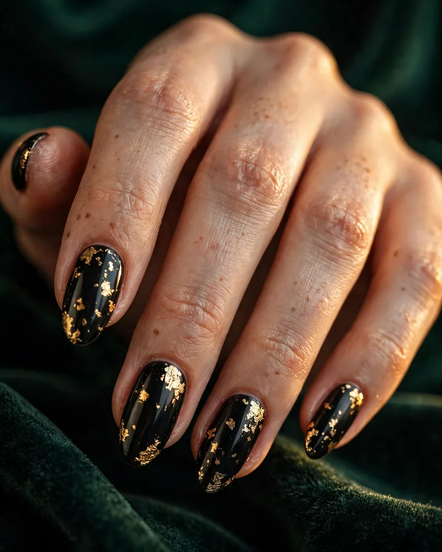 Glossy black almond nails with scattered gold foil flecks