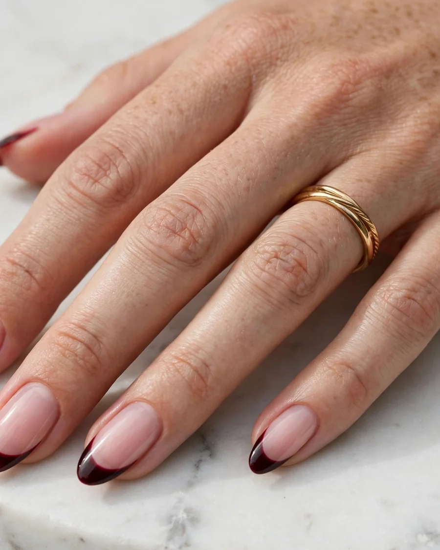 Cherry noir French tip almond nails with deep near-black red tips over sheer nude pink base